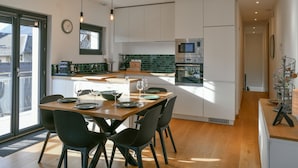 A modern kitchen with a dining area, featuring a large island, white cabinets, and a view through the glass door.