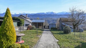 A paved pathway leading to a building with a metal roof, surrounded by greenery and a mountainous backdrop. - La Grangette Wifi Parking Terrace (Cruet)