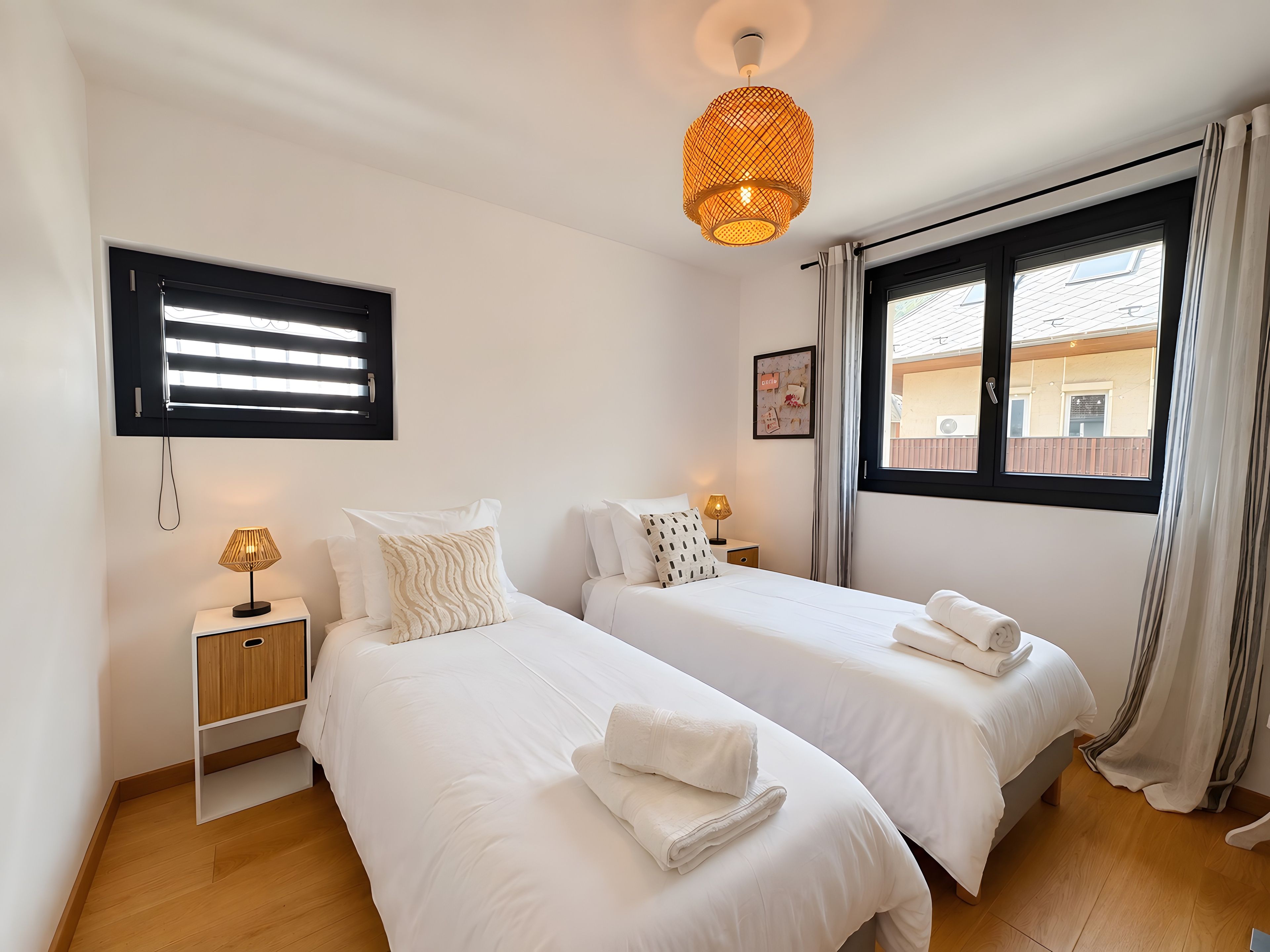 Habitación de hotel con dos camas, una mesita de noche con lámpara, una ventana con cortinas y un televisor montado en la pared.