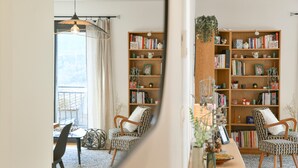 A room with a large wooden bookshelf, a dining table with chairs, and a view of the outdoors through a window. - La Grangette Wifi Parking Terrace (Cruet)