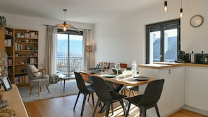 A modern kitchen with a dining area, wooden flooring, and a view through the window.