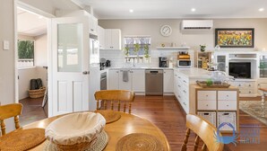 A modern kitchen with white cabinets, a dishwasher, and a microwave. There is a dining area with a wooden table and chairs, and a TV in the corner. - The Art Lovers Cottage in Mandurah 2BR (Dudley Park)