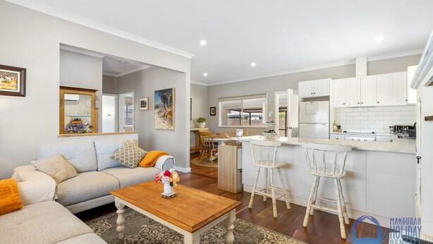 A modern living room with a sofa, coffee table, and a dining area with chairs. - The Art Lovers Cottage in Mandurah 2BR (Dudley Park)
