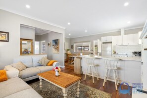 A modern living room with a sofa, coffee table, and a dining area with chairs. - The Art Lovers Cottage in Mandurah 2BR (Dudley Park)