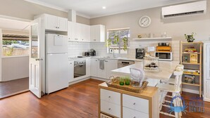A modern kitchen with white cabinetry, a central island, and a built-in oven. - The Art Lovers Cottage in Mandurah 2BR (Dudley Park)