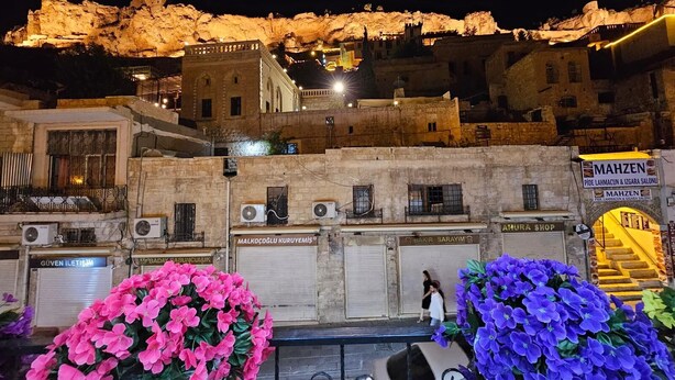 A historic building with stone walls and a balcony, surrounded by colorful flowers and a sign for 'MAHZEN'. - Hasan Pasa Konagi (Mardin)
