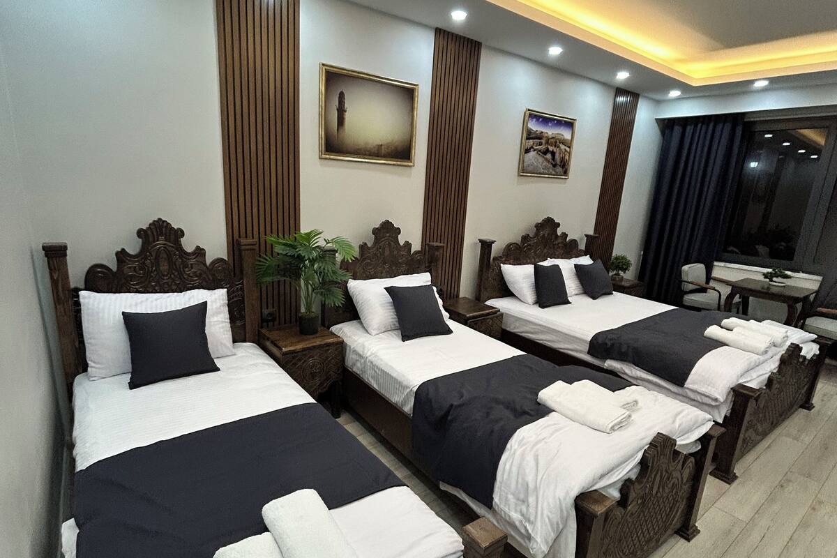 Une chambre d’hôtel avec trois lits en bois, chacun recouvert d’une courtepointe noire et blanche, et une petite table sur laquelle est posée une plante.