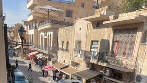 A yellow and black bus on a cobblestone street with buildings on either side, including a shop with a sign that reads "GÜVEN İLETİŞİM". - Hasan Pasa Konagi (Mardin)