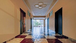 A corridor with patterned flooring and doors on both sides, leading to an open area with plants. - Hotel Grand Bella (Jaipur)