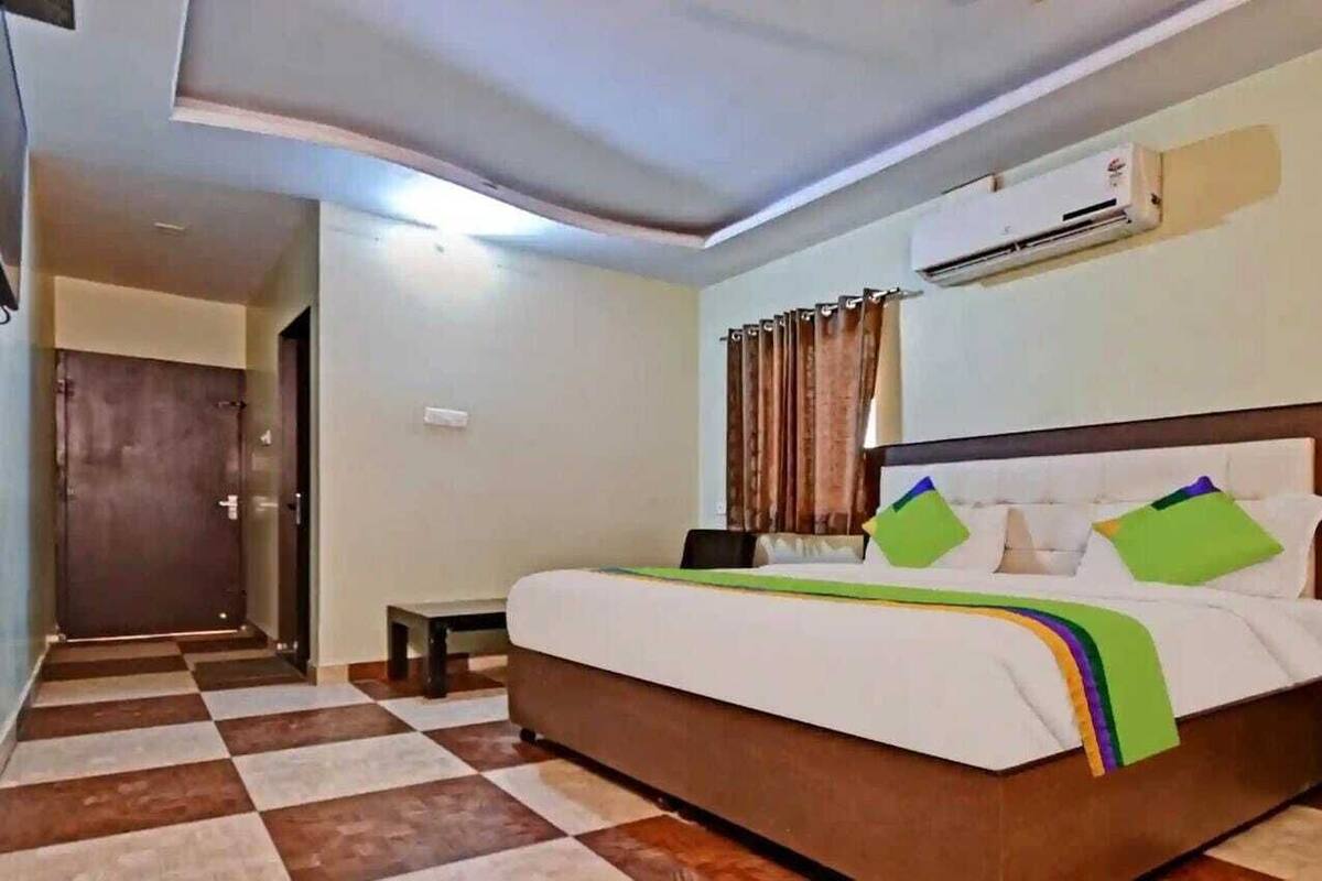 Ein Hotelzimmer mit Schachbrettmuster-Boden, einem Bett mit Holz-Kopfteil, einem kleinen Nachttisch und einer Klimaanlage an der Wand.
