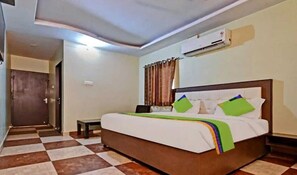Habitació d'hotel amb un sòl a escacs, un llit amb capçalera de fusta, una petita taula de nit i una unitat de climatització a la paret.