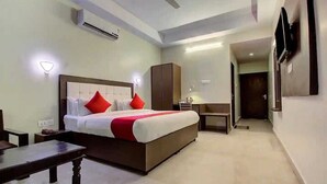 A hotel room with a bed, a desk, a wardrobe, and a TV mounted on the wall. - Hotel Grand Bella (Jaipur)
