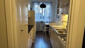 A narrow kitchen with white cabinets, a dining table, and a window with sheer curtains. - Charming Two Rooms Apartment in Stockholm (Stockholm)
