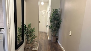 A hallway with wooden flooring, a dark mat at the entrance, and two potted plants. - Charming Two Rooms Apartment in Stockholm (Stockholm)
