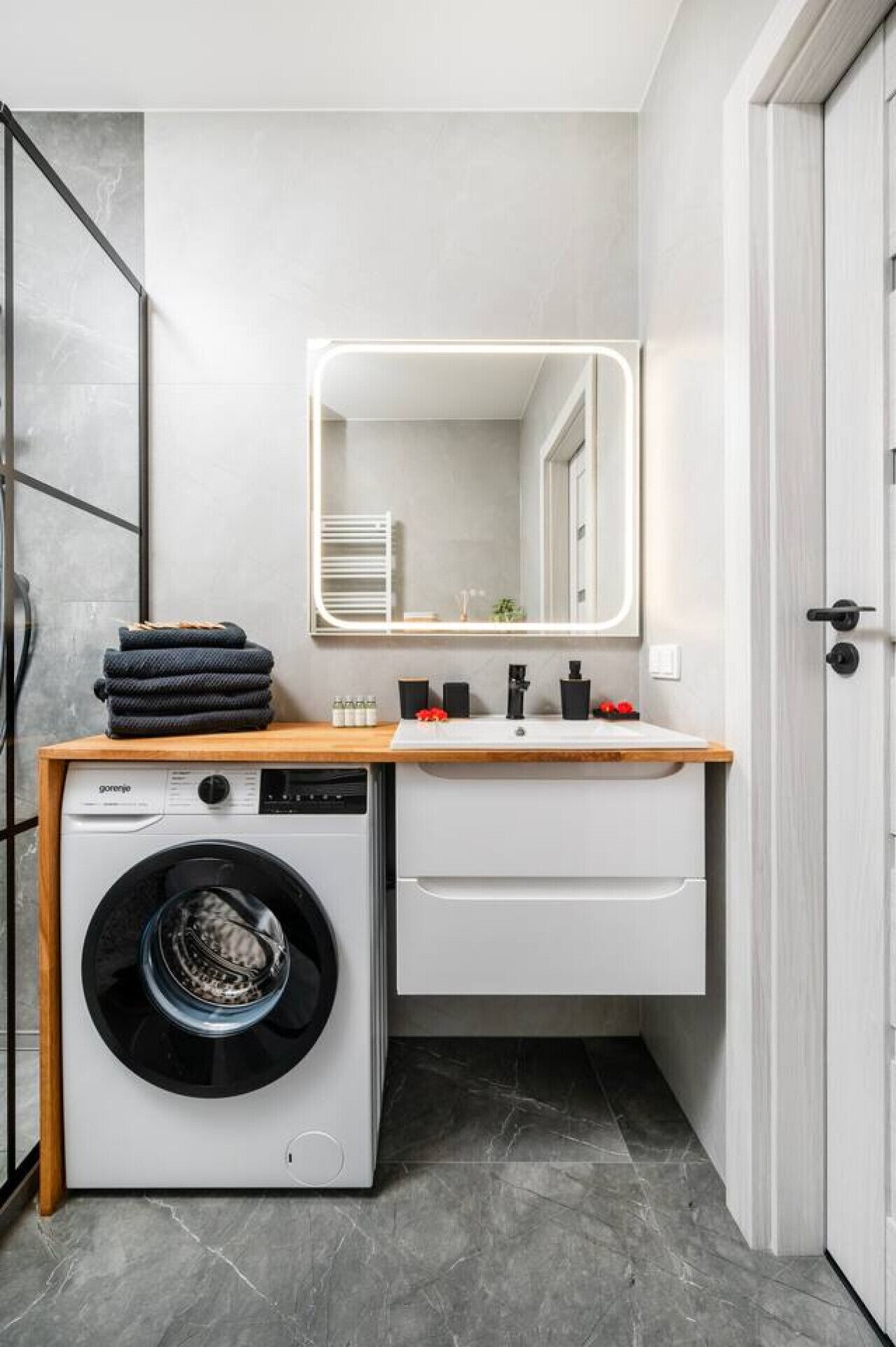 A compact laundry room with a washing machine, a sink, and a mirror.
