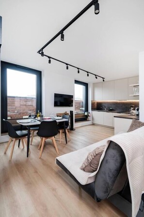 Un apartamento moderno con comedor, cocina y sala de estar. Cuenta con ventanas grandes, un televisor de pantalla plana y un diseño minimalista.