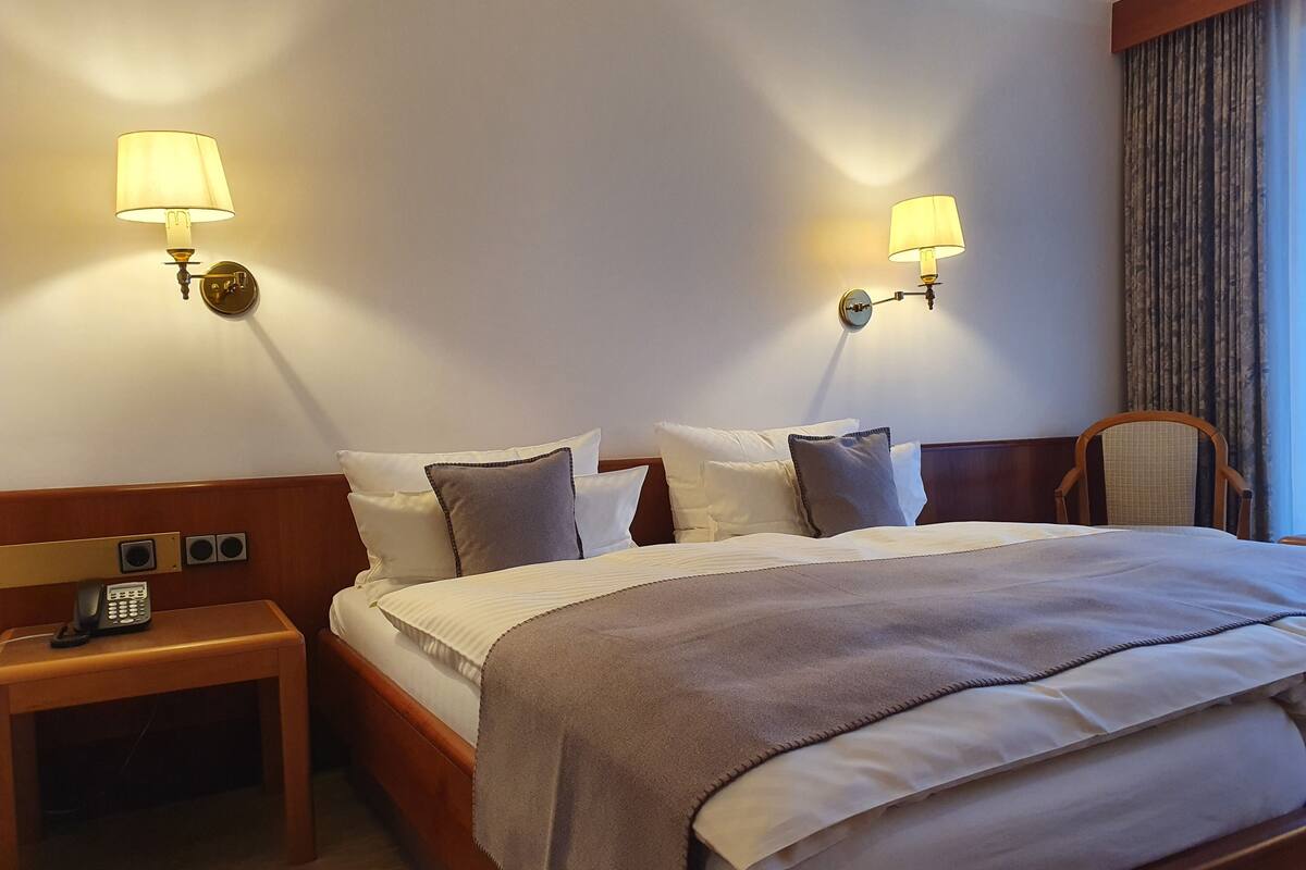 A hotel room with a bed, bedside tables, lamps, and a telephone.