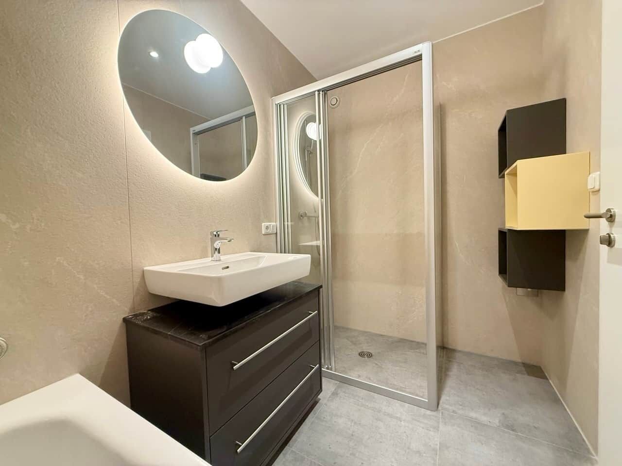 A modern bathroom with a glass shower enclosure, a white sink, and a dark vanity.
