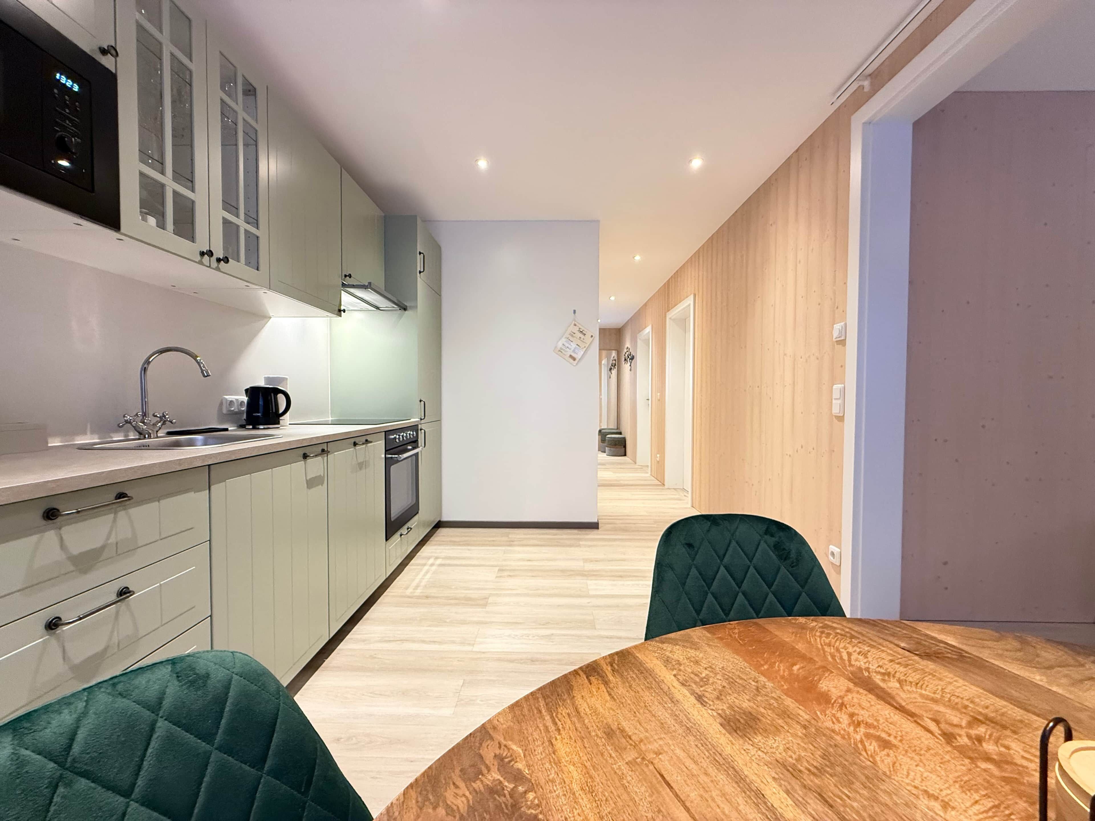 A modern kitchen with a wooden dining table and chairs, a built-in oven, and a coffee maker.