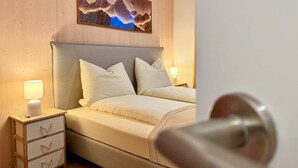 A hotel room with a wooden headboard, a bed with white bedding, a nightstand with a lamp, and a painting of mountains on the wall. - | 1 bedroom | Shower | (Grünau im Almtal)