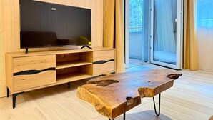 A modern living room with a flat-screen TV on a wooden TV stand, a wooden coffee table, and a sliding glass door leading to an outdoor area. - | 1 bedroom | Shower | (Grünau im Almtal)
