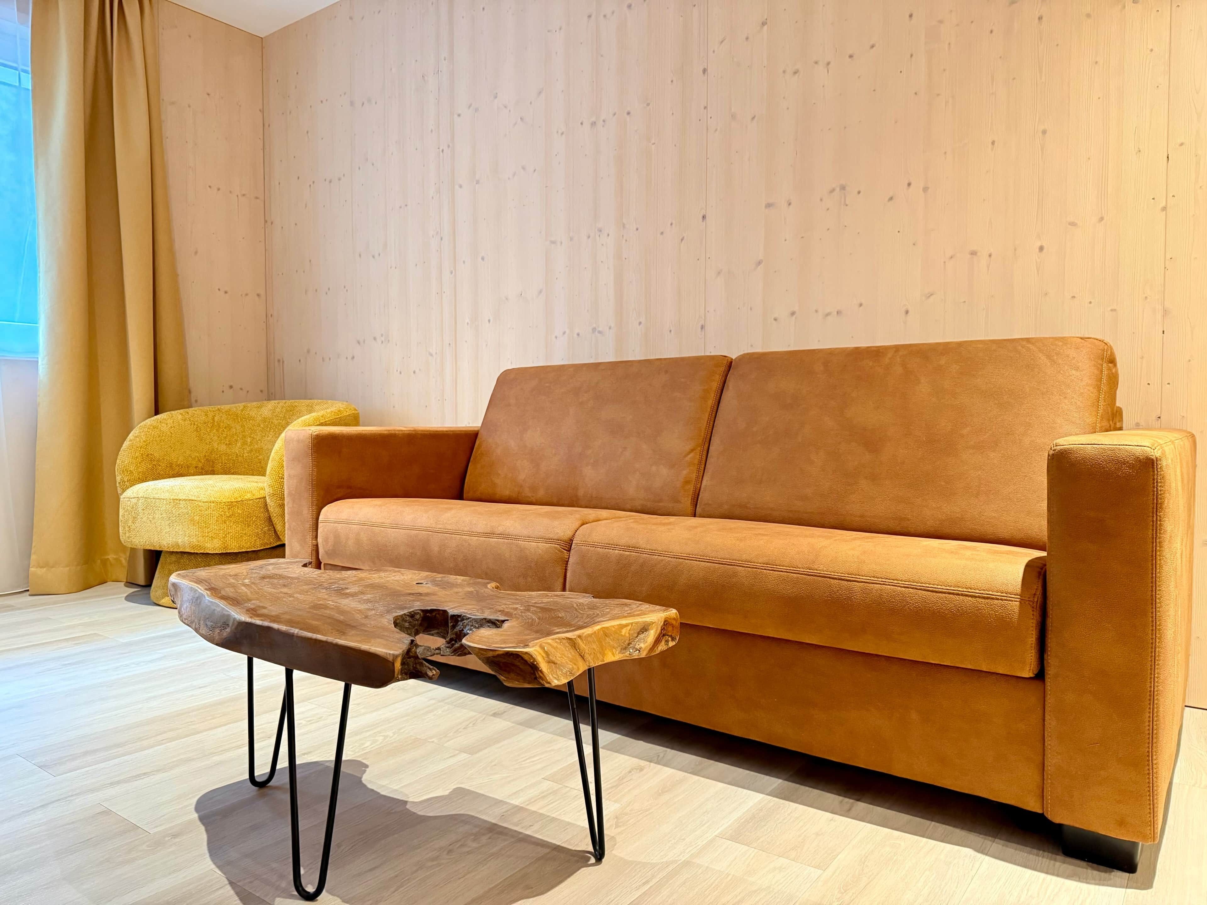 A room with a brown sofa, a yellow armchair, and a wooden coffee table with metal legs.