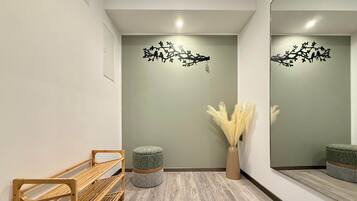A reception area with a wooden bench, a round ottoman, a vase with pampas grass, and wall art depicting birds on branches.