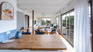 A modern kitchen with a wooden countertop, a kettle, and a telephone. There is a dining area with a table and chairs, and a sofa in the background. - Walk to Beach | Pet Friendly | Sleep 5 (Ocean Grove)