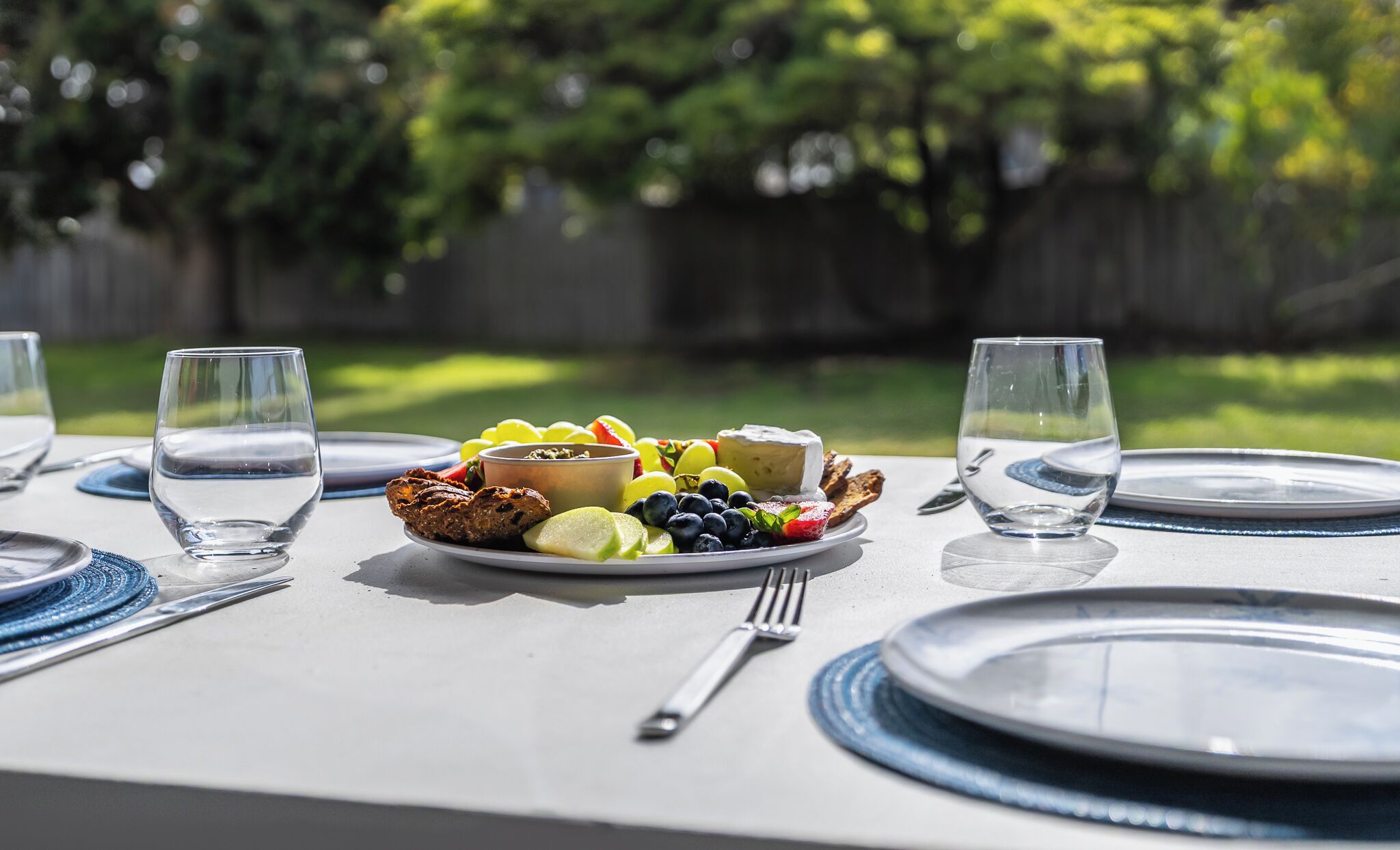 A table set for a meal with plates, cutlery, and a bowl of fruit and cheese.