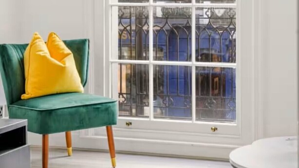 A room with a large window, a green chair with yellow cushions, and a round table. - Chic Beauchamp Place Home (London)