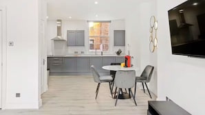 A modern kitchen with grey cabinets, a central island, and a dining area with a round table and grey chairs. - Chic Beauchamp Place Home (London)