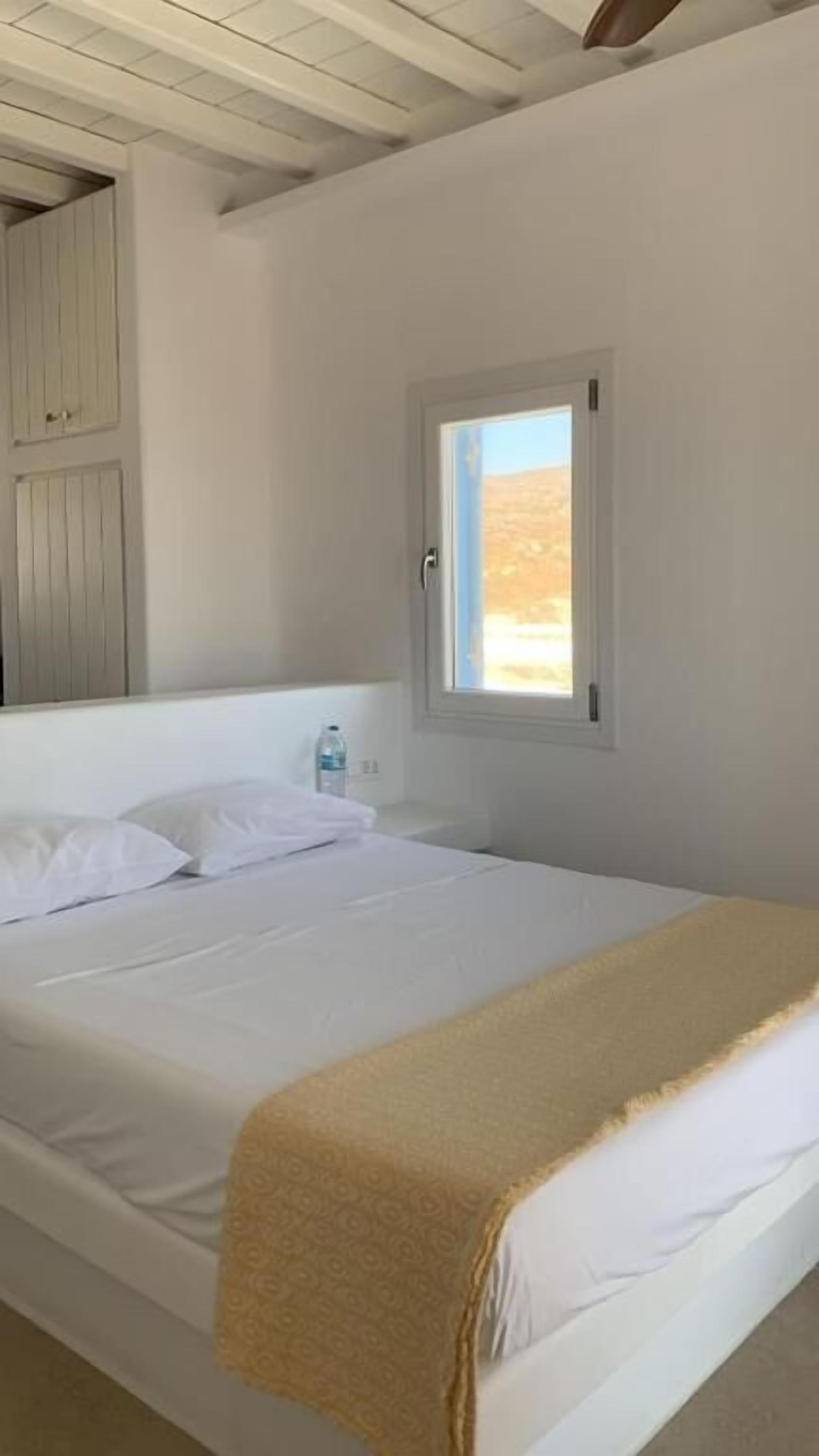 A single-bed room with a white bedspread, a beige throw blanket, and a window with a view of a desert landscape.