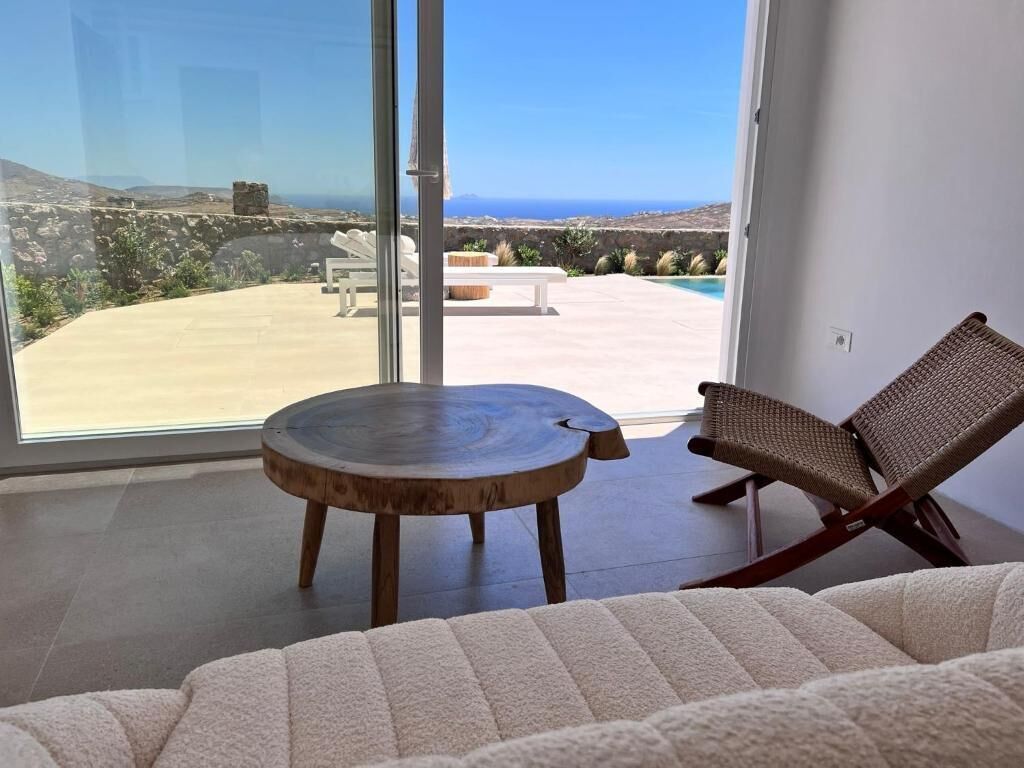 A modern living room with a large glass door leading to a patio with a pool and a view of the sea.