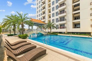 Una piscina amb gandules, un pont i un edifici d'alguns pisos amb balcons.