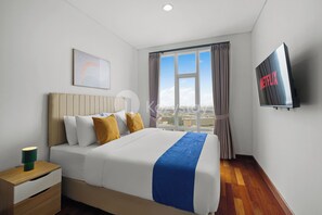 Habitació d'hotel amb un llit, televisió, finestra amb cortines i vista a la ciutat.