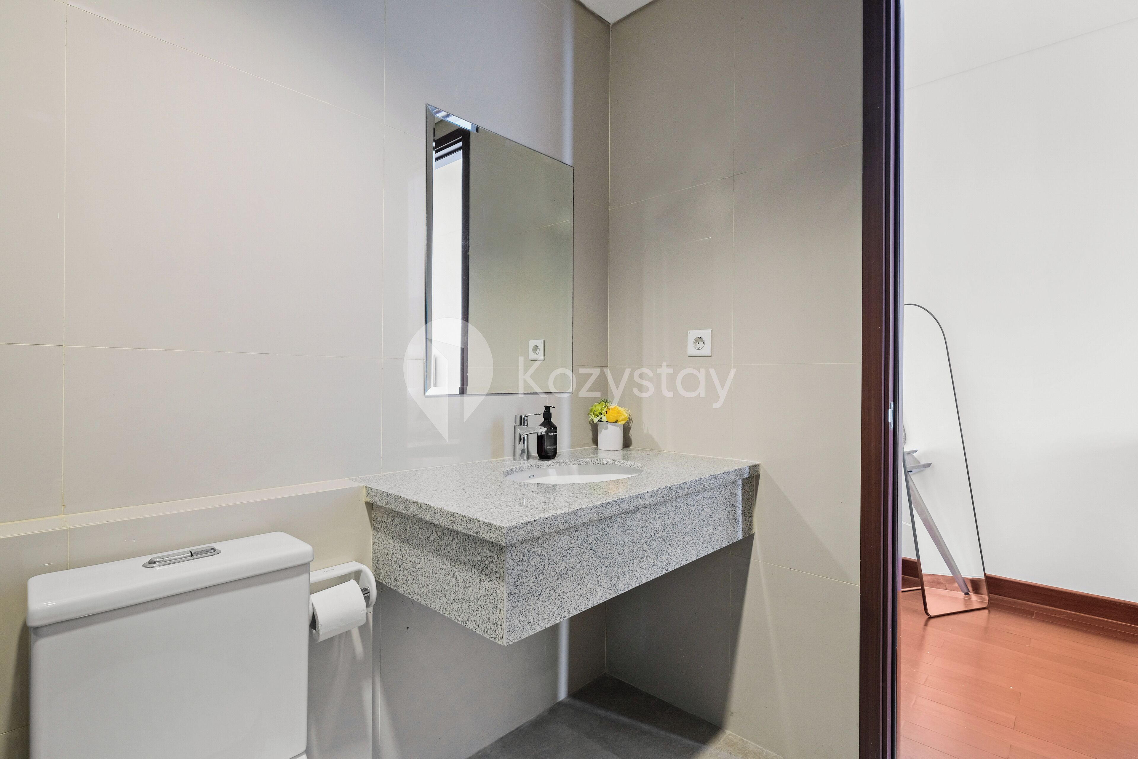 A modern bathroom with a granite countertop, a toilet, and a mirror.
