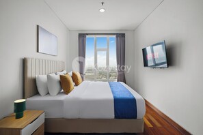 Habitació d'hotel amb un llit gran, una televisió, una taula de nit i una finestra amb cortines.
