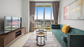Ein modernes Wohnzimmer mit einem Flachbildfernseher, einem grünen Sofa, einem kleinen runden Tisch und einem Balkon mit Blick.