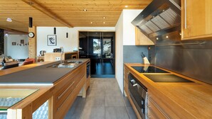 Une cuisine moderne avec des meubles en bois, une hotte en acier inoxydable et un grand îlot central doté d’un plan de travail en verre.