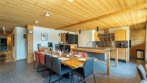 Une cuisine moderne avec des meubles en bois, un coin repas avec une table et des chaises en bois, et une horloge visible au mur.