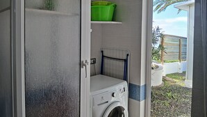 Ein Waschbereich mit Waschmaschine, Wäscheständer und einem grünen Behälter auf einem Regal.