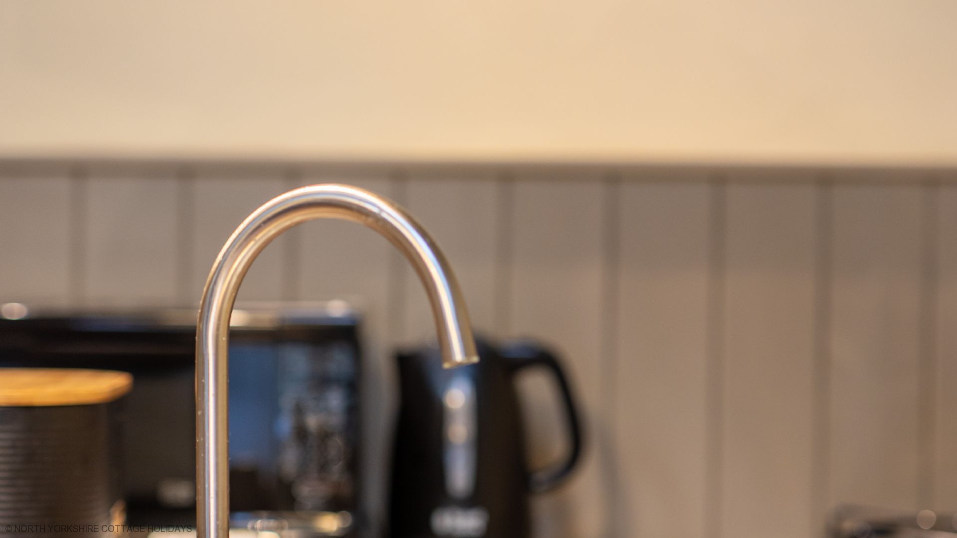 A modern kitchen with a stainless steel faucet, a coffee maker, and a kettle.