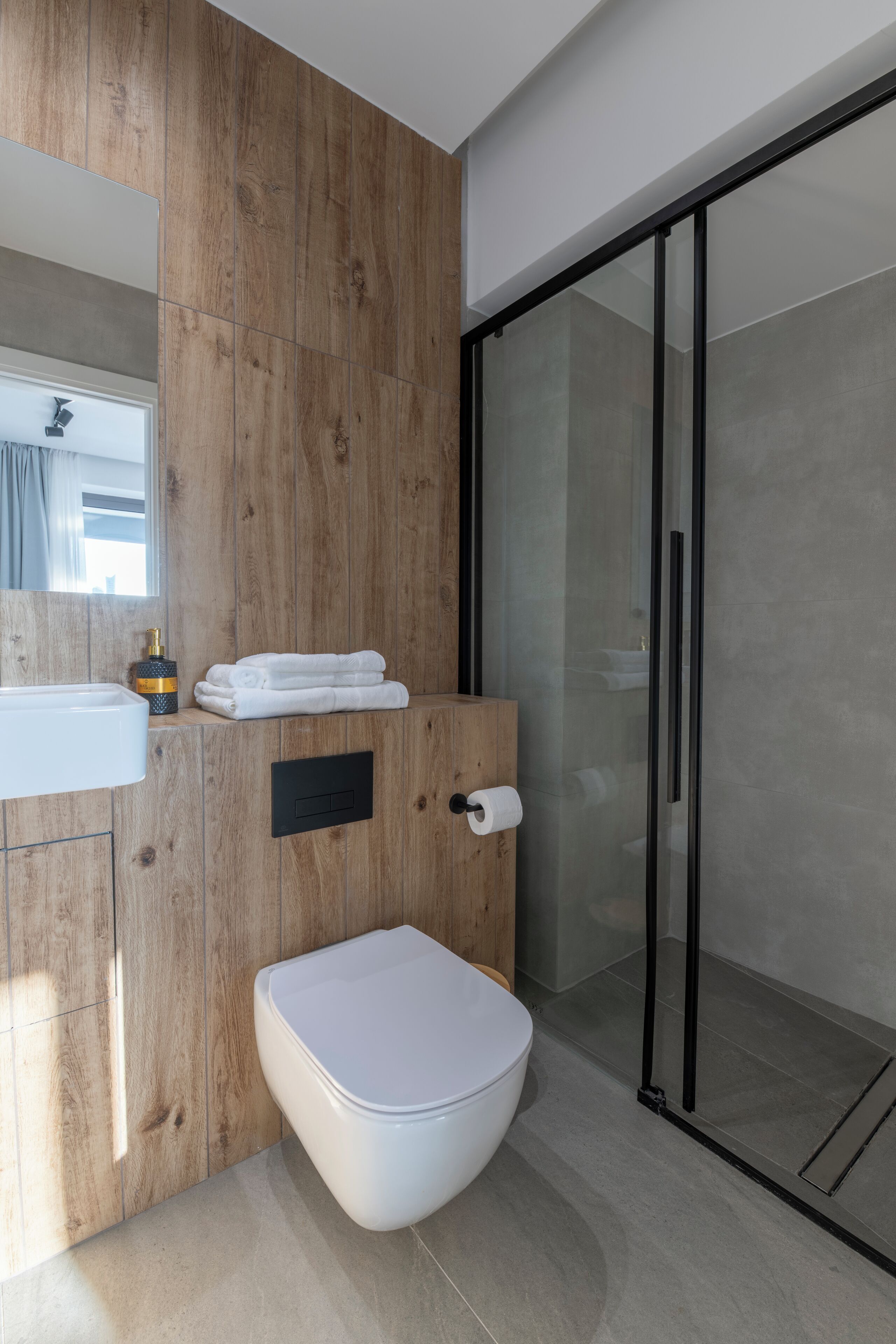 Een moderne badkamer met een houten wastafelmeubel, toilet en een douchecabine met glazen wanden.