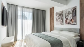 Ein modernes Schlafzimmer mit einem großen Bett, einem Nachttisch und einem an der Wand montierten Fernseher.