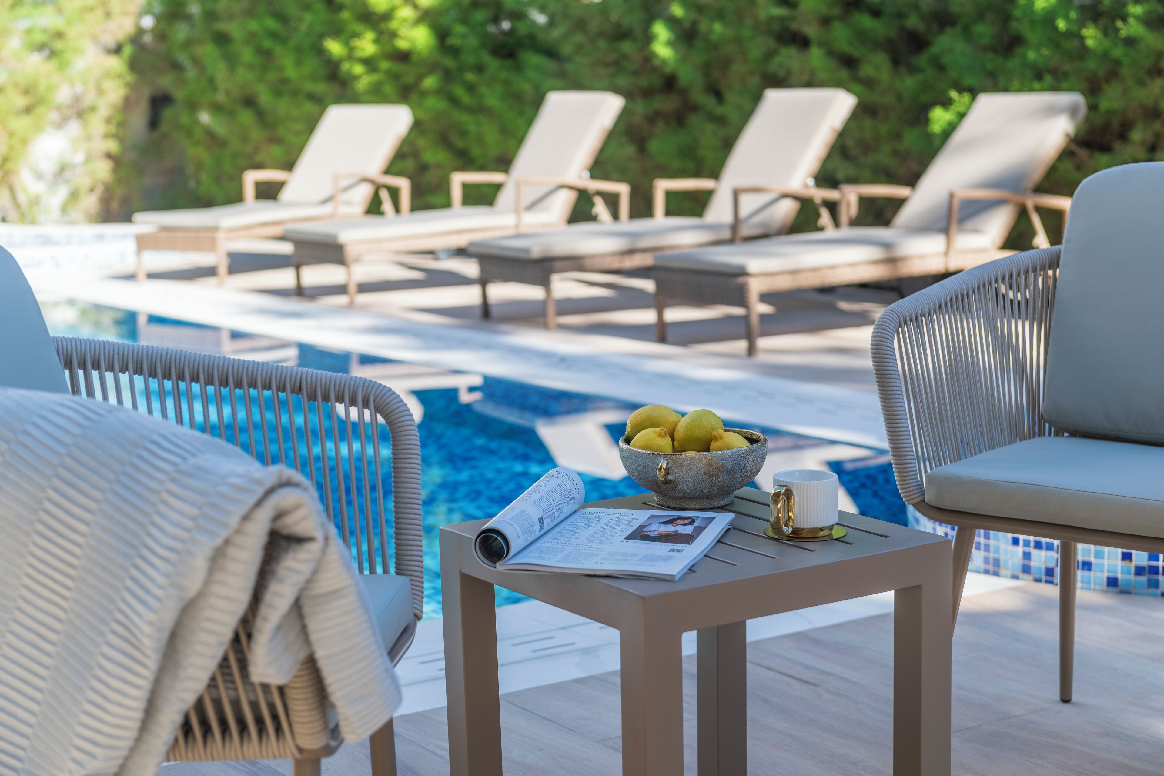 A poolside area with lounge chairs, a table with a bowl of lemons, and a newspaper.