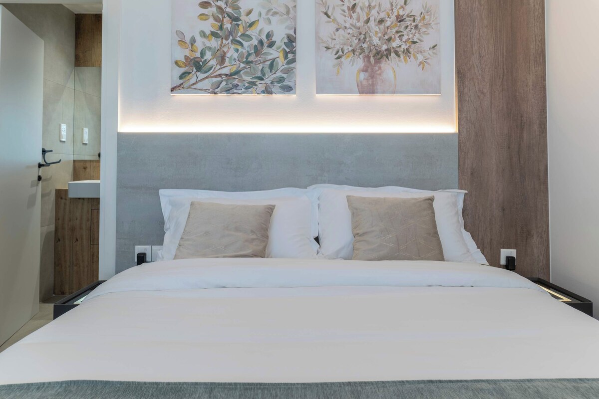 A modern hotel room with a large bed, two wall-mounted paintings, a wooden headboard, and a small bedside table.