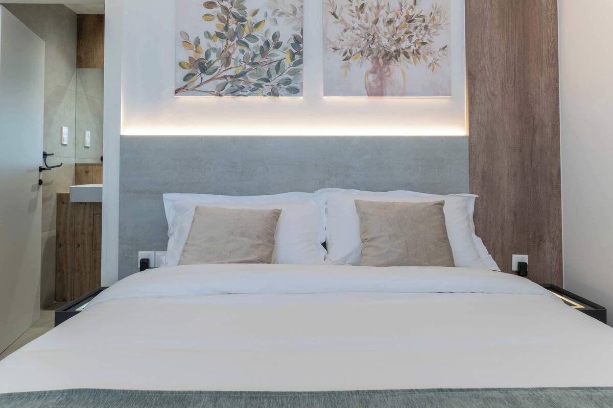 Una camera d'albergo moderna con un letto grande, due quadri appesi al muro, una testiera in legno e un comodino.