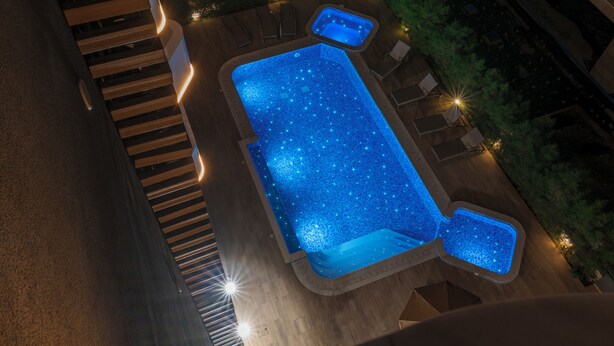 Ein rechteckiger Pool mit Sterneneffekt, umgeben von einer Holzterrasse und Liegestühlen.