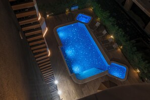 A rectangular swimming pool with a starry effect, surrounded by wooden deck and lounge chairs. - 26 Suites Limassol (Limassol)