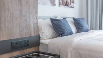 Une chambre d’hôtel avec une tête de lit en bois, un lit avec une literie blanche et bleue, une table de chevet avec une télécommande et une prise électrique murale.